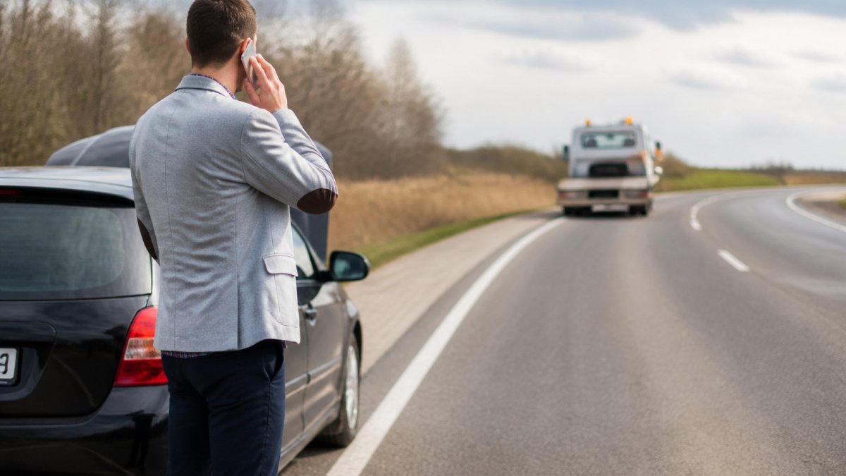 Driver calling for roadside assistance as a tow truck approaches to provide insurance cover towing on the highway.